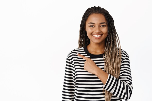 Image of smiling young black woman pointing finger left showing copy space promo sale standing over white background