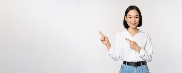 Image of smiling young office lady asian business entrepreneur pointing fingers left showing client