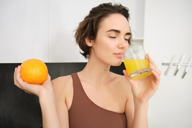 Image of sportswoman fitness girl holding glass of juice and an orange smiling drinking vitamin beve