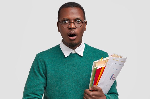 Image of stupefied male employee holds papers with financial report and diagrams, scientific literature, prepares for having business lessons