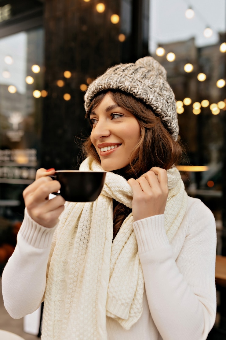 Free Photo image of styling european woman in knitted cap and scarf drinking coffee and enjoying time outside in winter