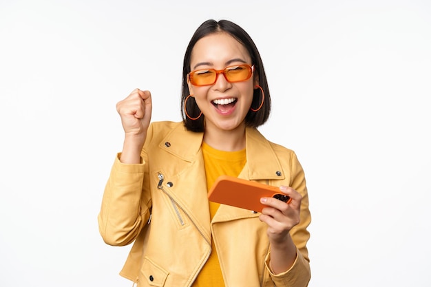 Image of stylish korean girl dancing with smartphone laughing happy and smiling standing over white background