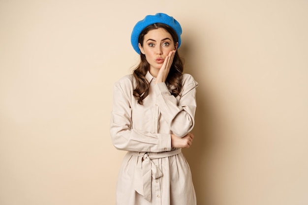 Image of stylsh beautiful woman looking surprised shocked reaction at camera posing in trench coat a...