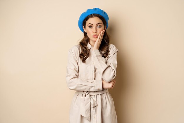 image of stylsh beautiful woman looking surprised shocked reaction at camera posing in trench coat a...