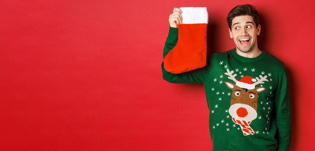 プレゼントやクリスマスの靴下を見て、緑のセーターを着て驚いて面白がっている男の画像...