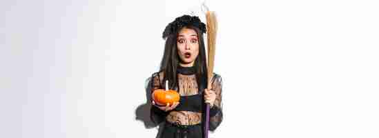 Foto gratuita l'immagine della ragazza asiatica sorpresa che boccheggiava si chiedeva e fissava la telecamera indossando il costume da strega su halloween