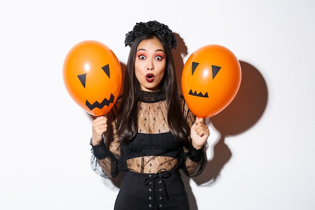 怖い顔で風船を持って、ハロウィーンを祝う魔女の衣装で驚いたアジアの女性の画像