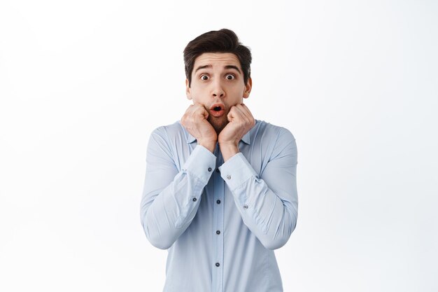 Image of surprised and excited businessman say wow, gasping and looking fascinated at camera, impressed by promo deal, standing against white background