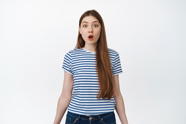 Image of surprised girl drop jaw say wow and stare in awe at camera standing impressed against white background