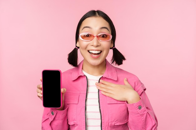 ピンクの背景に立っている携帯電話アプリ画面スマートフォンディスプレイアプリケーションインターフェイスを示す驚いた女の子の画像
