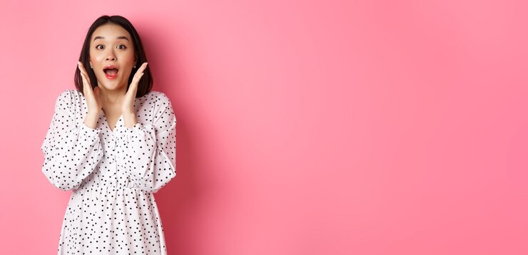 無料Photo ドレスの女性モデルを着た驚いた韓国人の女の子がカメラを見つめ、あえぎながら立っているovの画像