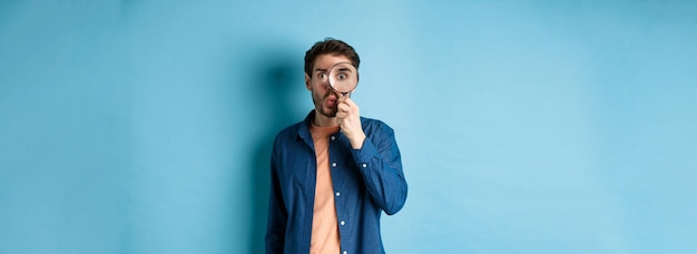 Free photo image of surprised man found something interesting say wow and look through magnifying glass standin