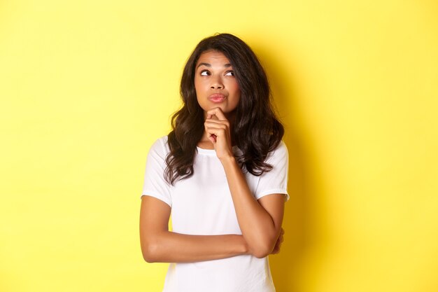 Image of thoughtful beautiful african american girl making her choice looking at upper right corner