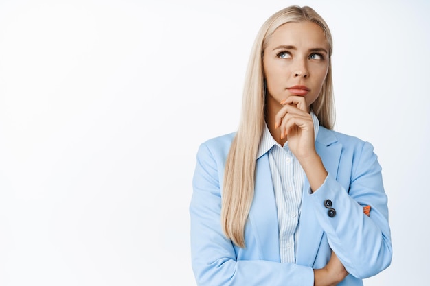 Image of thoughtful corporate woman looking aside thinking with serious face standing in suit over white background