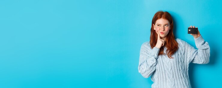 मुफ़्त फोटो image of thoughtful redhead girl thinking about shopping showing credit card and pondering standing
