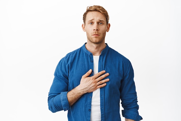 Image of touched redhead man hold hand on heart, melting from cuteness and something beautiful, contemplating lovely moment, standing heartfelt against white background