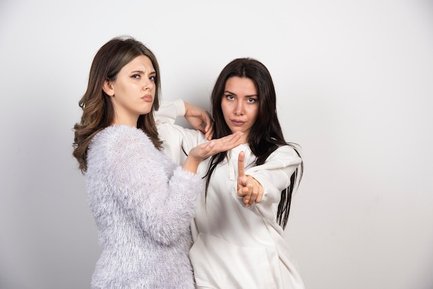 Image of two best friends standing together and looking at camera on white wall .