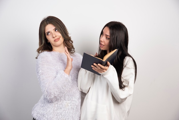 Free photo image of two best friends standing together and posing with book on white wall .