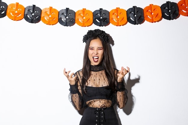 Image of wicked witch laughing evil and grimacing, woman celebrating halloween against party decorations, standing over pumpkin streamers.