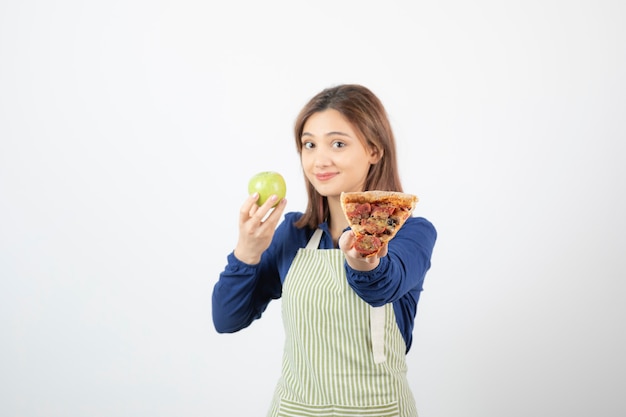 Image of woman in apron trying to choose what to eat apple or pizza