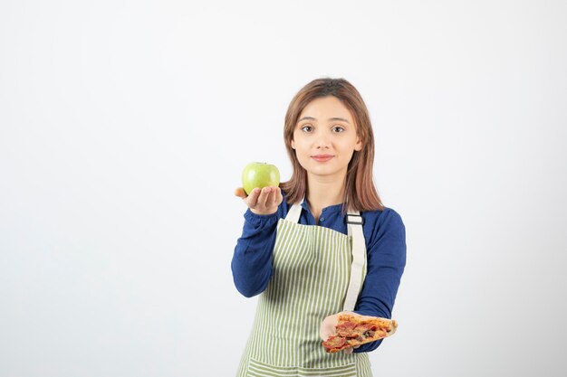 image of woman in apron trying to choose what to eat apple or pizza