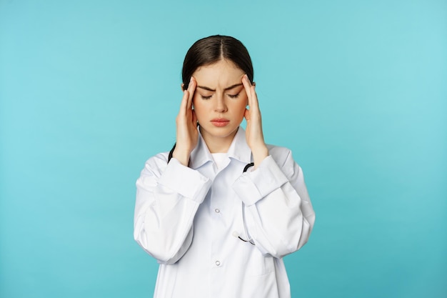 Image of woman doctor medical personel grimacing from discomfort having headache migraine feeling de...