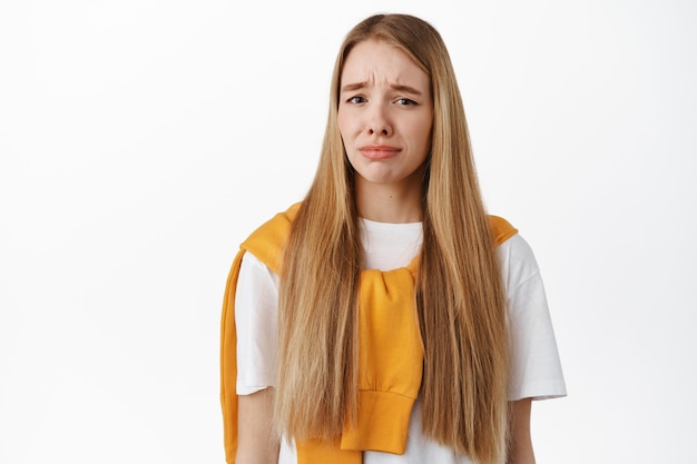 Image of woman feeling gross or pity, grimacing from dislike and disgust, frowning upset, standing against white wall