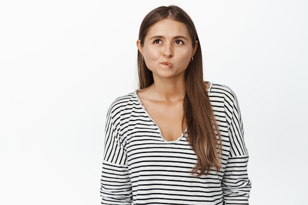 Image of woman thinking, pucker lips and looking up as if making choice, deciding, standing pensive against white background