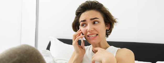 Foto gratuita immagine di una donna con un'espressione facciale imbarazzata e ansiosa che parla al telefono cellulare.