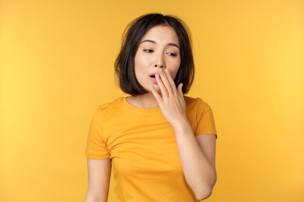 Image of young asian girl student yawning feeling tired standing sleepy agaisnt yellow background Copy space