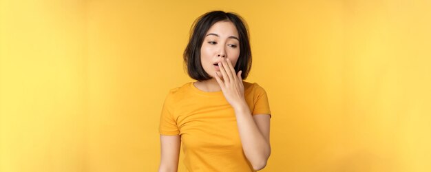 Image of young asian girl student yawning feeling tired standing sleepy agaisnt yellow background