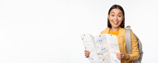 Image of young asian girl tourist traveller with map and backpack posing against white studio background