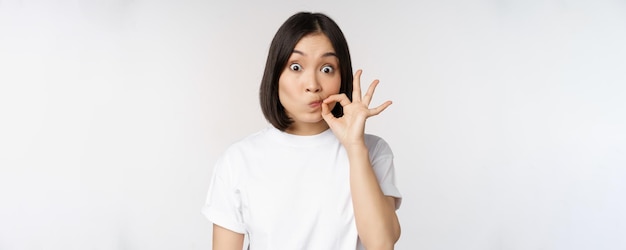 Image of young asian woman showing silence gesture zipping mouth seal lips make promise standing ove
