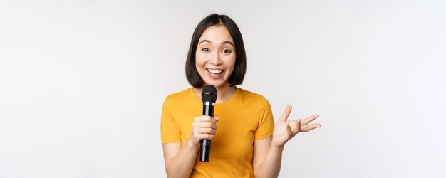 Free photo image of young asian woman talking in microphone perfom with mic giving speech standing in yellow tshirt against white background