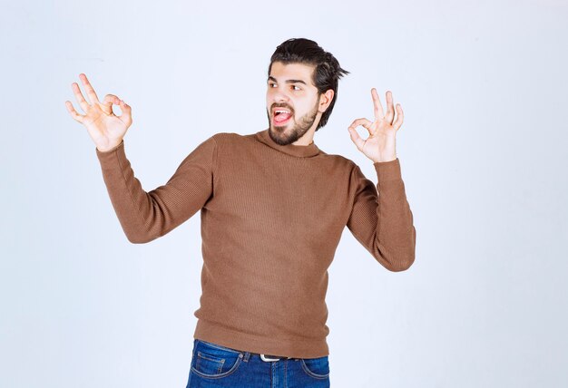 Изображение молодого привлекательного человека, одетого в коричневый свитер, показывая одобренный жест. Фото высокого качества