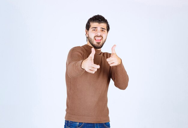 Image of young attractive man dressed in brown sweater showing thumbs up gesture.