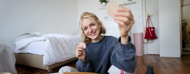 Image of young blond woman girl records video about makeup shows skin tone beauty products sits in a