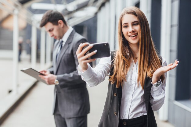 若いビジネス仲間のカップルが携帯電話で自分撮りをしている画像。