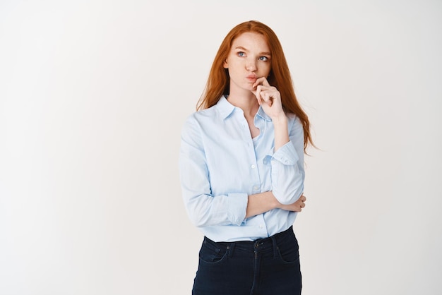 Image of young businesswoman thinking Redhead girl in blue shirt making decision looking thoughtful at upper left corner white background