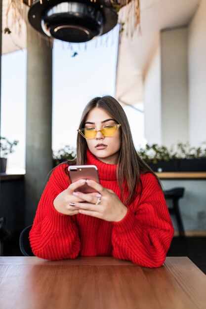 Изображение молодой женщины, читающей смс по телефону в кафе