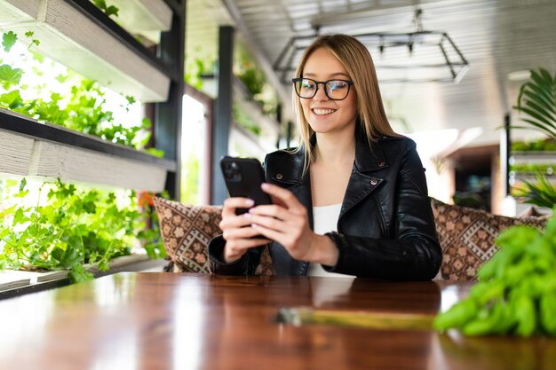 カフェで電話でSMSを読んでいる若い女性の画像