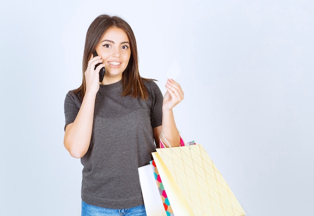 Foto gratuita immagine di una giovane ragazza che parla al telefono e tiene in mano le borse della spesa.