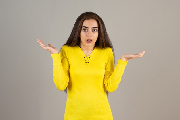 Image of young girl in yellow top standing and posing  on gray wall.