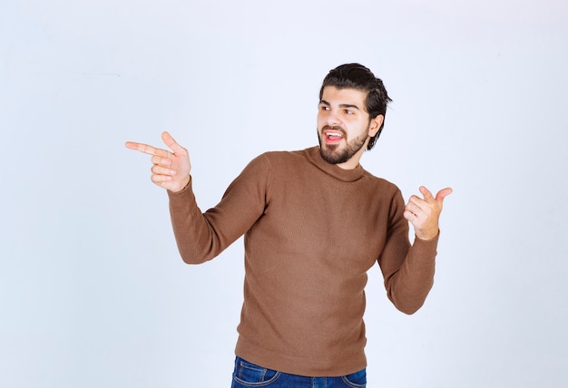 Image of a young handsome man model standing and pointing away with fingers. High quality photo