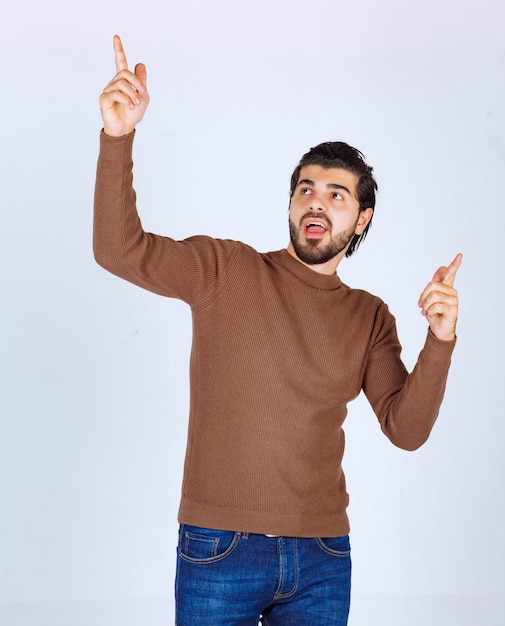 Image of a young handsome man model standing and pointing up with fingers. High quality photo