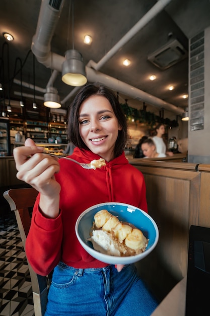 Изображение молодой счастливой улыбающейся женщины с удовольствием и едой мороженого в кафе или ресторане крупным планом портрет