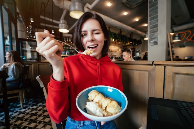 Изображение молодой счастливой улыбающейся женщины с удовольствием и едой мороженого в кафе или ресторане крупным планом портрет