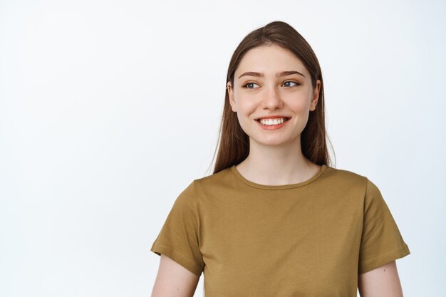 Image of young hopeful woman smiling happy, looking aside at empty space on white