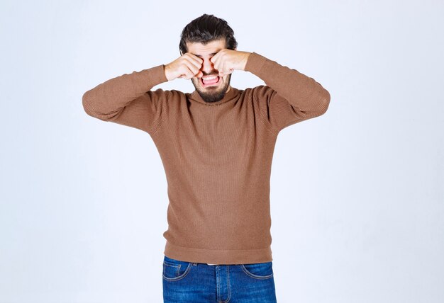 Image of young male model in brown sweater standing over white wall.