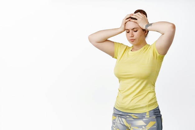 Free photo image of young plus size girl workout in gym doing fitness holding hands on head looking tired of exercises white background